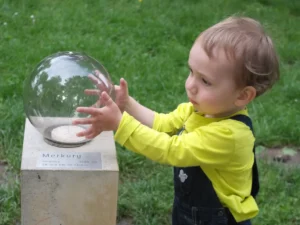 Ogród dla dzieci. Na zdjęciu dziecko trzymające przezroczystą kulę w ogrodzie doświadczeń.